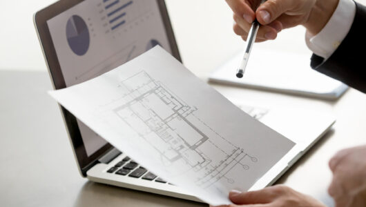 Male hand holding project plan, statistics on screen, close up Close up view of male hand holding project plan, financial statistics data on laptop screen at background, analyzing real estate market, mortgage loan with low rate, construction investment